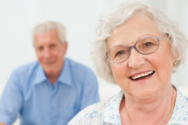 Iamge of  an older couple with the male blurred in the background behind smiling lady